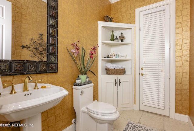 half bath featuring toilet, baseboards, a sink, and tile patterned floors