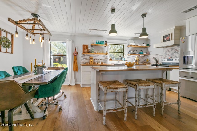 kitchen featuring a kitchen breakfast bar, pendant lighting, stainless steel fridge, backsplash, and white cabinetry