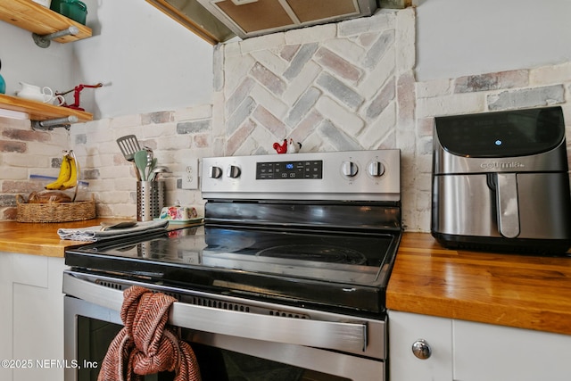 kitchen featuring stainless steel electric range, wooden counters, tasteful backsplash, exhaust hood, and white cabinetry