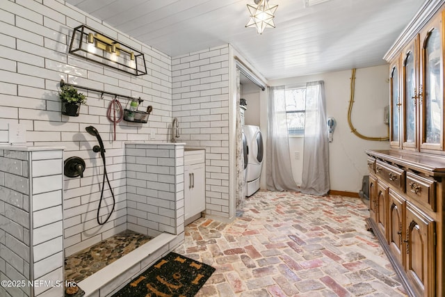 bathroom with independent washer and dryer, tiled shower, and sink