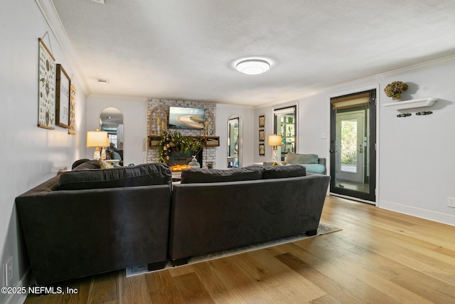 living room with light hardwood / wood-style floors, a textured ceiling, a stone fireplace, and ornamental molding