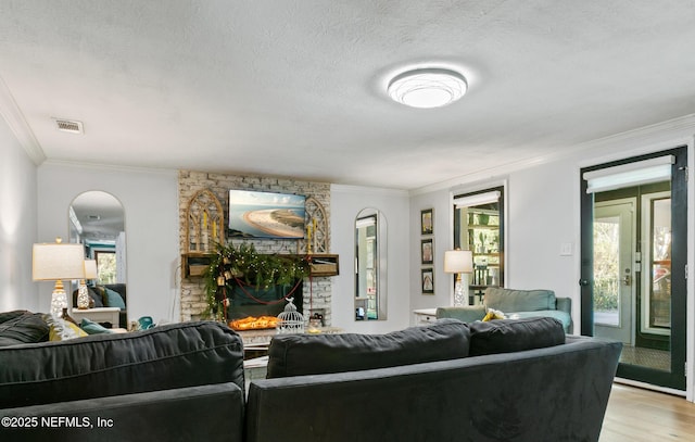 living room with light wood-type flooring, crown molding, a brick fireplace, and a textured ceiling