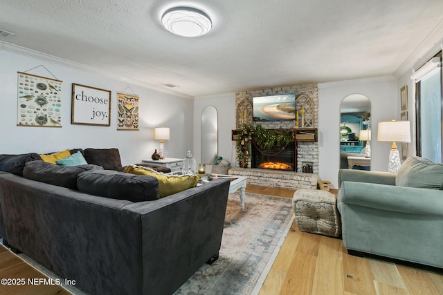 living room with light hardwood / wood-style floors, crown molding, a brick fireplace, and a textured ceiling