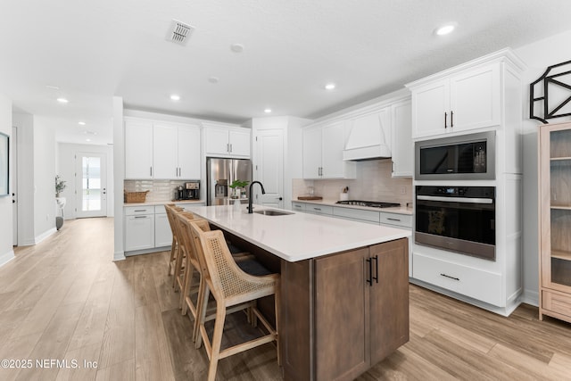 kitchen featuring white cabinetry, light countertops, custom exhaust hood, black appliances, and a center island with sink