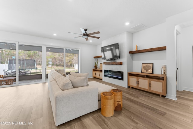 living room with light wood-type flooring, a glass covered fireplace, visible vents, and recessed lighting