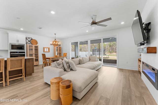 living room with light wood-type flooring, a glass covered fireplace, baseboards, and recessed lighting