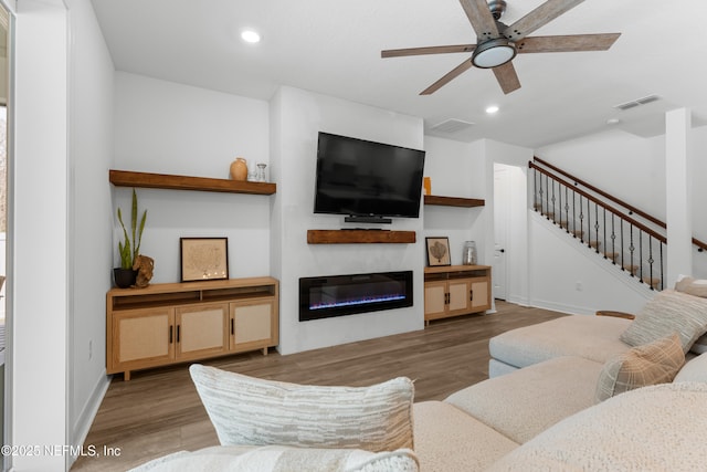 living area with stairway, visible vents, wood finished floors, and a glass covered fireplace