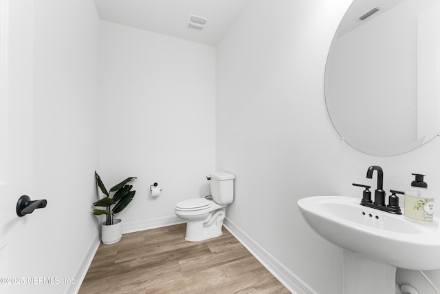 bathroom featuring toilet, a sink, visible vents, wood finished floors, and baseboards