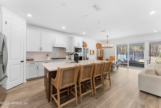 kitchen with white cabinets, light countertops, a center island with sink, and pendant lighting