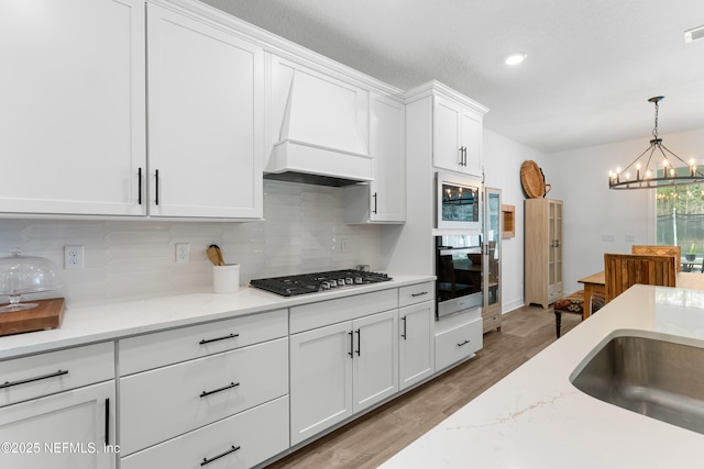 kitchen with stainless steel gas cooktop, premium range hood, white cabinets, tasteful backsplash, and pendant lighting