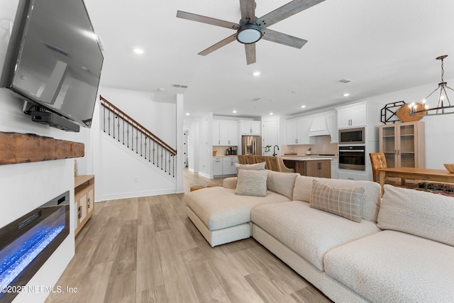 living room with light wood finished floors, recessed lighting, visible vents, stairway, and ceiling fan with notable chandelier