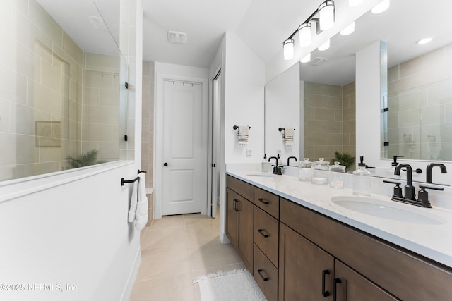 full bath with double vanity, tiled shower, a sink, and tile patterned floors