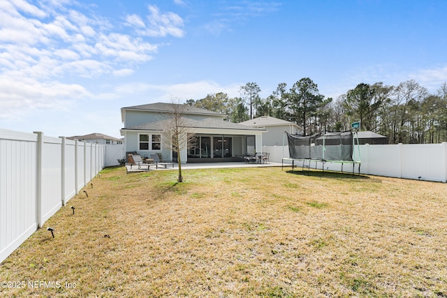 rear view of house with a trampoline, a yard, a sunroom, a patio area, and a fenced backyard