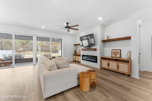 living room with recessed lighting, a glass covered fireplace, light wood finished floors, and ceiling fan