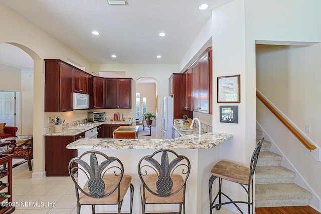 3383 Olympic Dr, Green Cove Springs, FL 32043 - kitchen featuring arched walkways, white appliances, a peninsula, and reddish brown cabinets