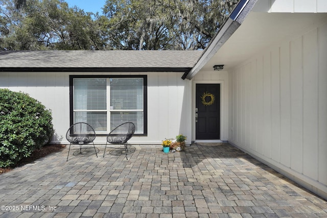 entrance to property featuring roof with shingles and a patio