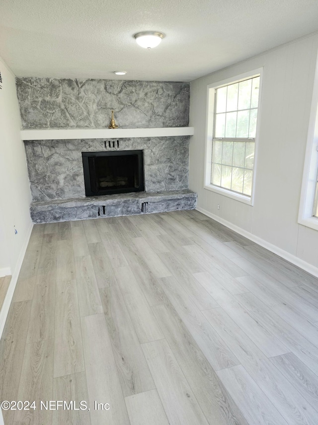 unfurnished living room featuring a fireplace, light hardwood / wood-style floors, and a textured ceiling