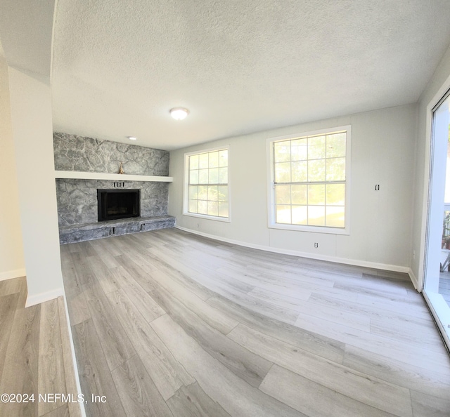 unfurnished living room featuring a textured ceiling, a stone fireplace, and light hardwood / wood-style floors