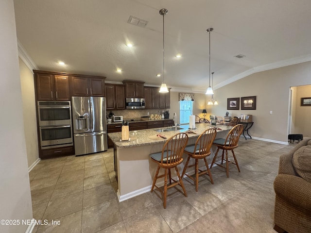 kitchen with appliances with stainless steel finishes, dark brown cabinets, a kitchen breakfast bar, and light stone countertops