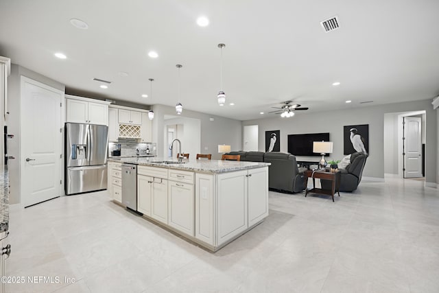 kitchen featuring hanging light fixtures, appliances with stainless steel finishes, white cabinetry, a sink, and an island with sink