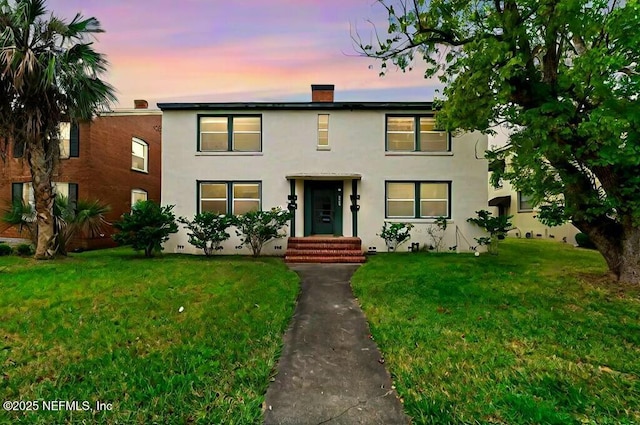 view of front of house featuring crawl space, stucco siding, a chimney, and a yard