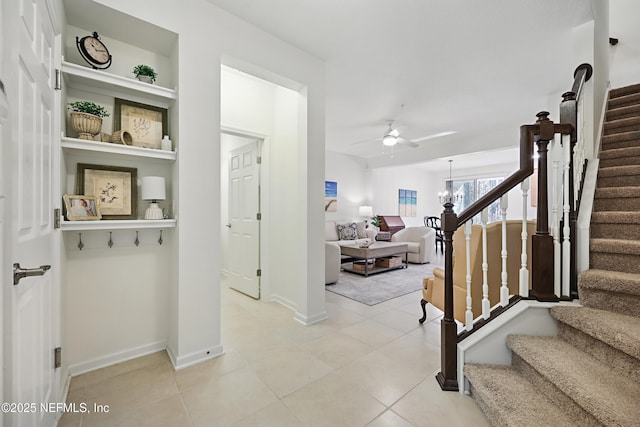 interior space with baseboards, ceiling fan with notable chandelier, stairway, and light tile patterned flooring