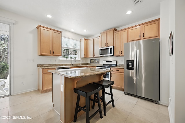 kitchen with light tile patterned floors, a kitchen island, light stone counters, a breakfast bar, and stainless steel appliances