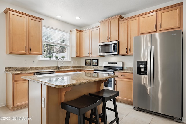 kitchen featuring a breakfast bar, a sink, a kitchen island, appliances with stainless steel finishes, and light stone countertops