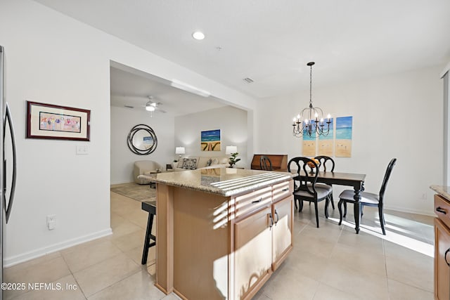 kitchen with light tile patterned floors, stone countertops, a breakfast bar area, open floor plan, and hanging light fixtures