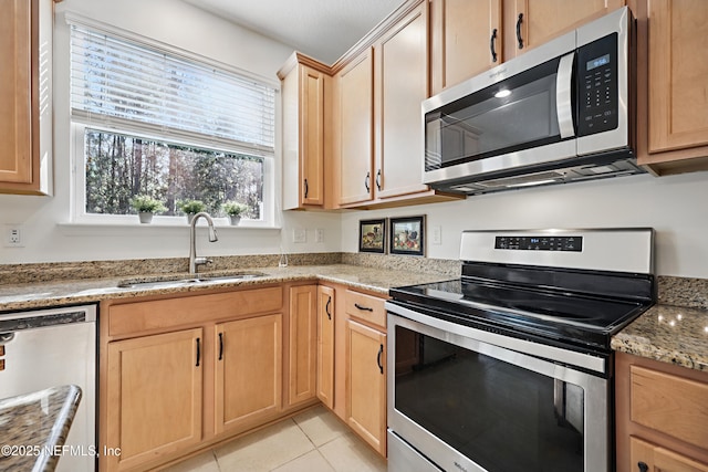 kitchen with light tile patterned floors, a sink, appliances with stainless steel finishes, light stone countertops, and light brown cabinetry