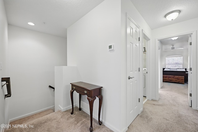 hallway with light carpet, baseboards, a textured ceiling, and an upstairs landing