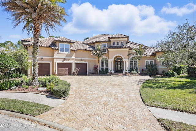 mediterranean / spanish home featuring a garage, a tile roof, decorative driveway, a front lawn, and stucco siding