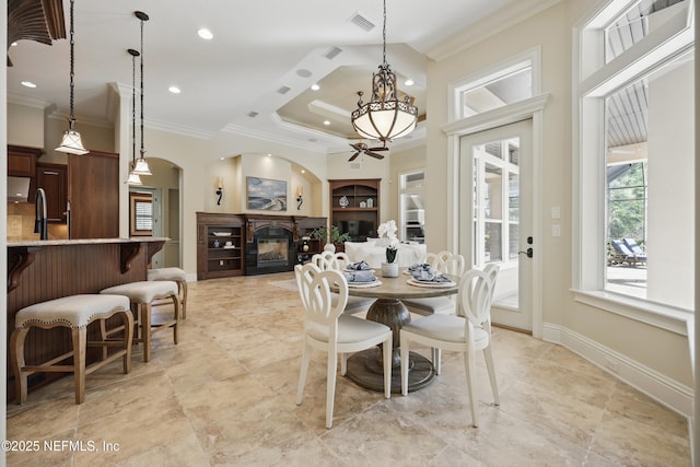 dining room with arched walkways, visible vents, ornamental molding, a glass covered fireplace, and baseboards