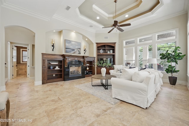 living room with a raised ceiling, visible vents, ornamental molding, a glass covered fireplace, and baseboards