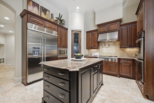 kitchen with backsplash, ornamental molding, a kitchen island, built in appliances, and under cabinet range hood