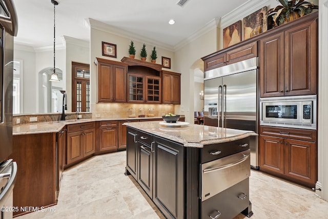 kitchen featuring pendant lighting, crown molding, backsplash, light stone countertops, and built in appliances