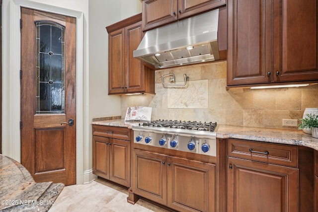 kitchen featuring tasteful backsplash, stainless steel gas stovetop, under cabinet range hood, and light stone counters