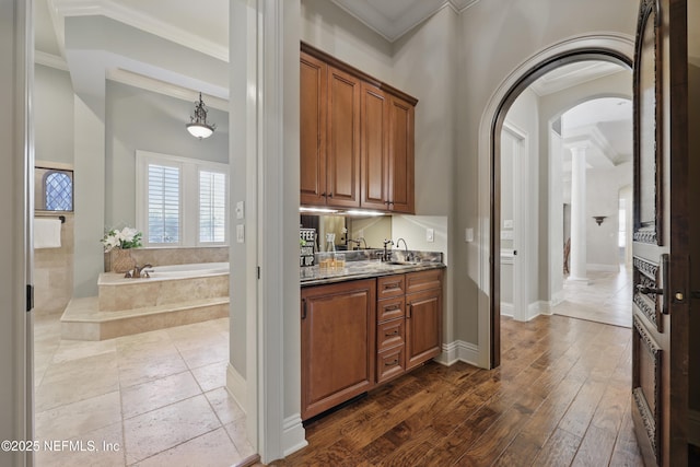 bar with arched walkways, dark wood finished floors, crown molding, a sink, and baseboards