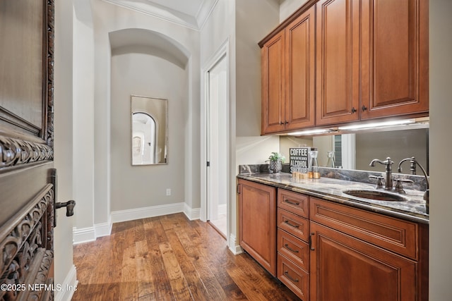 interior space with baseboards, arched walkways, wood finished floors, crown molding, and a sink