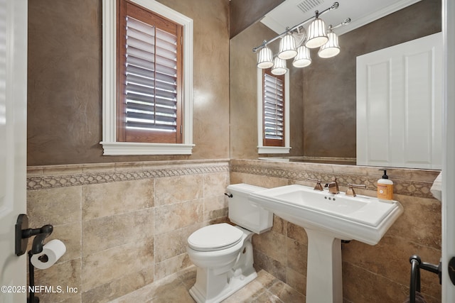 bathroom featuring toilet, a healthy amount of sunlight, tile walls, and a wainscoted wall