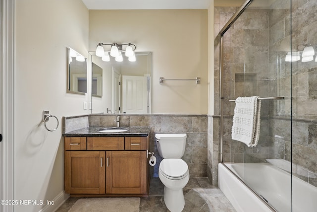 bathroom featuring bath / shower combo with glass door, toilet, tile patterned flooring, vanity, and tile walls