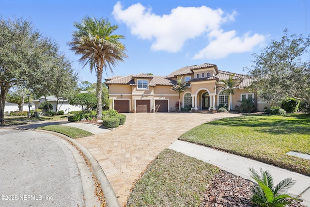 mediterranean / spanish home featuring decorative driveway, stucco siding, a garage, a tiled roof, and a front lawn