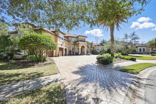 mediterranean / spanish-style home featuring decorative driveway, a tiled roof, and stucco siding