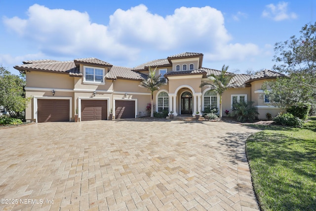 mediterranean / spanish house featuring decorative driveway, a tile roof, stucco siding, a garage, and a front lawn