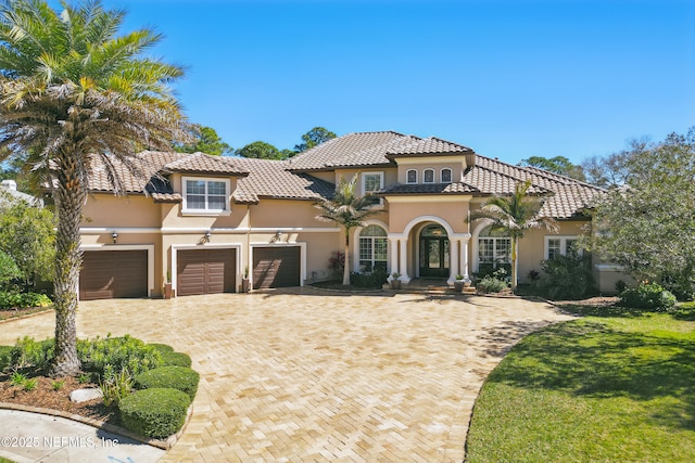 mediterranean / spanish-style house with a tiled roof, a front lawn, decorative driveway, and stucco siding