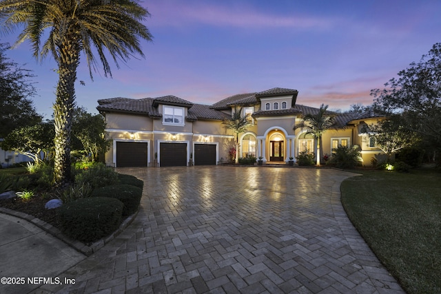 mediterranean / spanish house with an attached garage, a tile roof, decorative driveway, and stucco siding