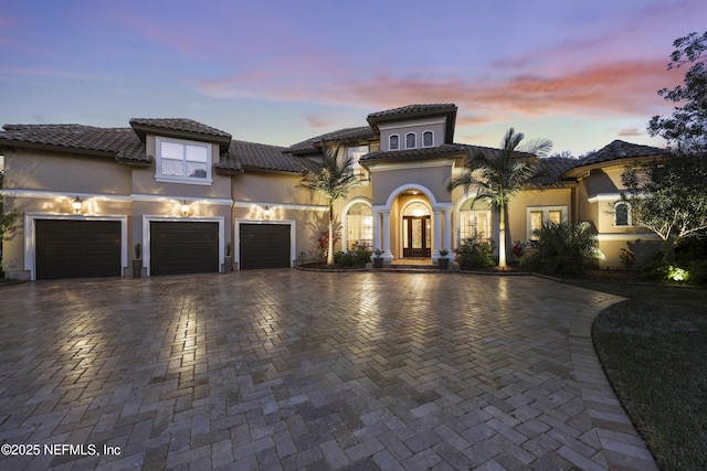 mediterranean / spanish-style house featuring a tiled roof, decorative driveway, an attached garage, and stucco siding