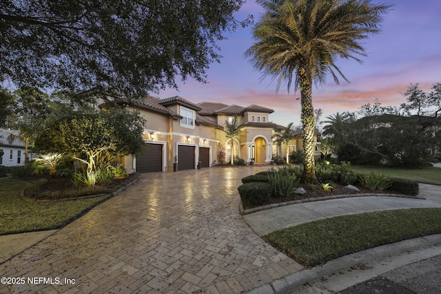 mediterranean / spanish house featuring a garage, decorative driveway, a tile roof, and stucco siding