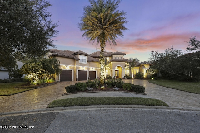 mediterranean / spanish house with an attached garage, a tiled roof, decorative driveway, and stucco siding