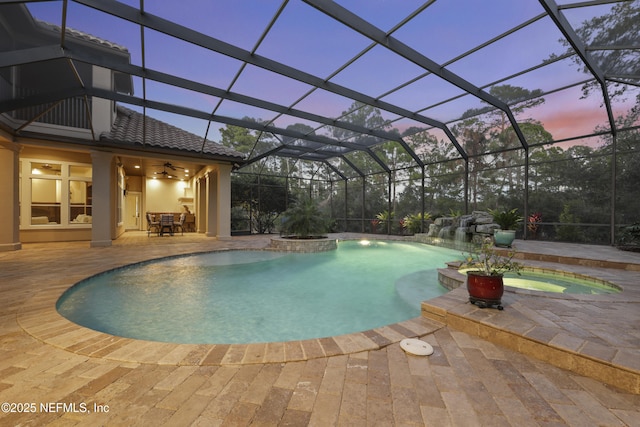 pool at dusk featuring a patio, glass enclosure, and a pool with connected hot tub